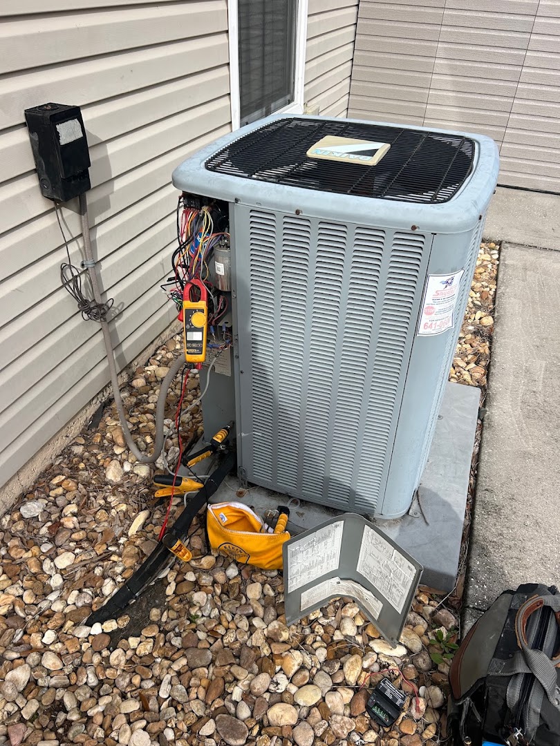 Technician testing a residential condenser unit beside a home